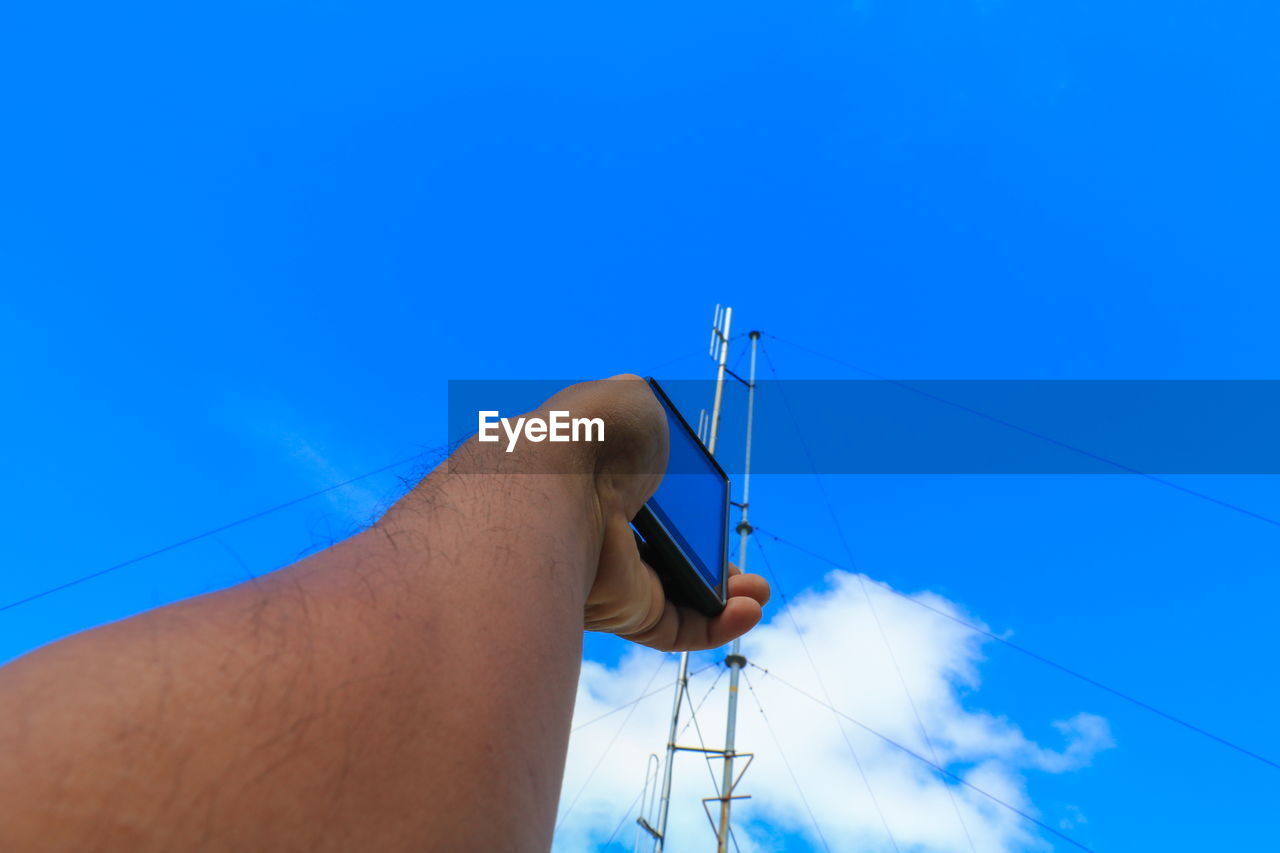 Cropped man holding smart phone by communications tower