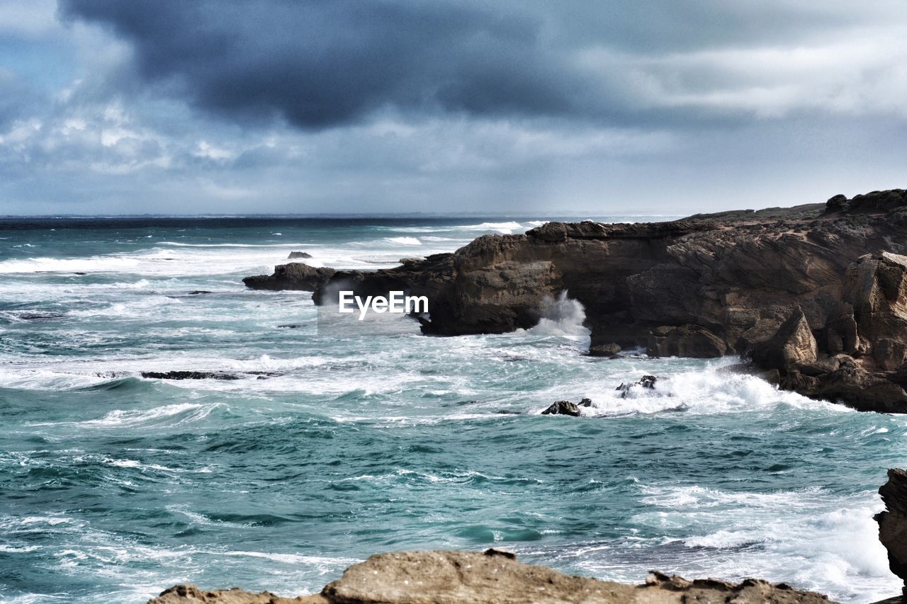 Scenic view of sea by rock formations against cloudy sky