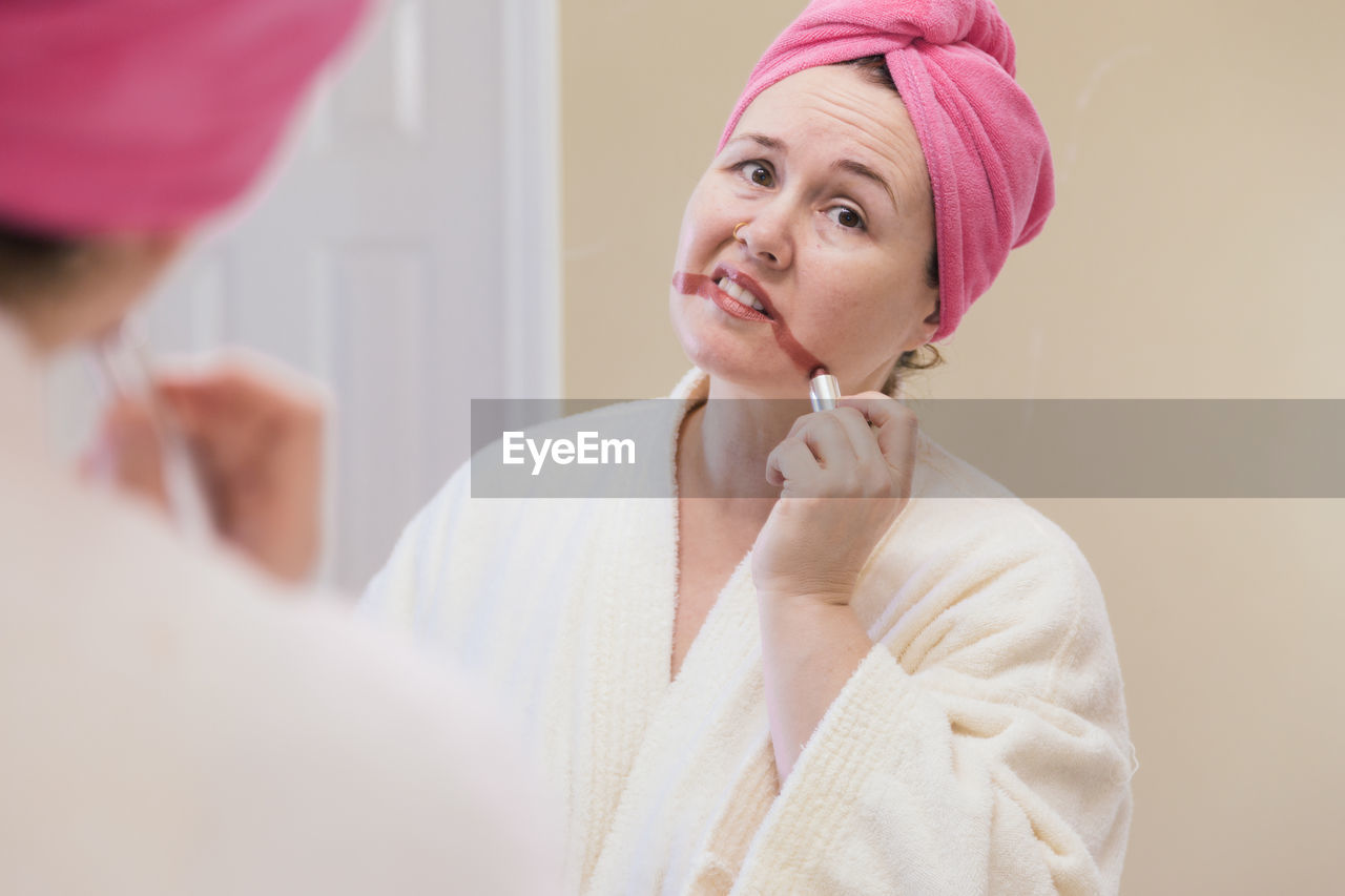 Mature woman applying lipstick reflecting on mirror