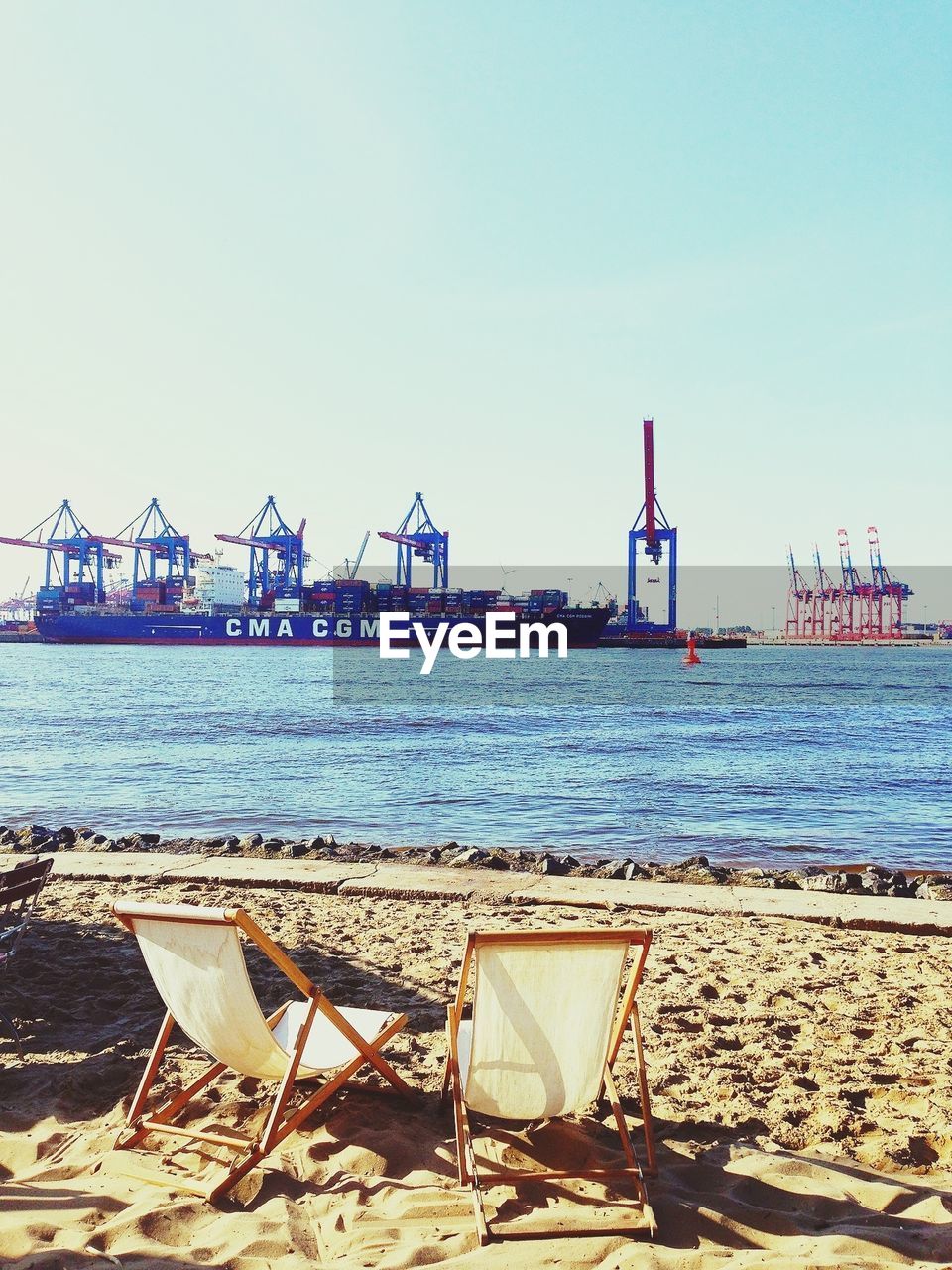 Container ship docked at port with empty deck chairs in foreground