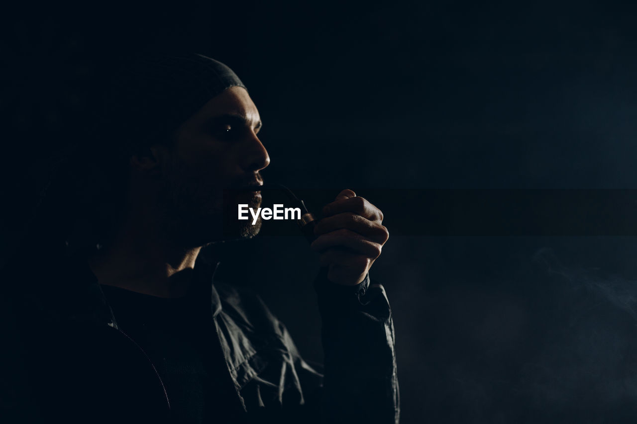 Portrait of young man smoking over black background