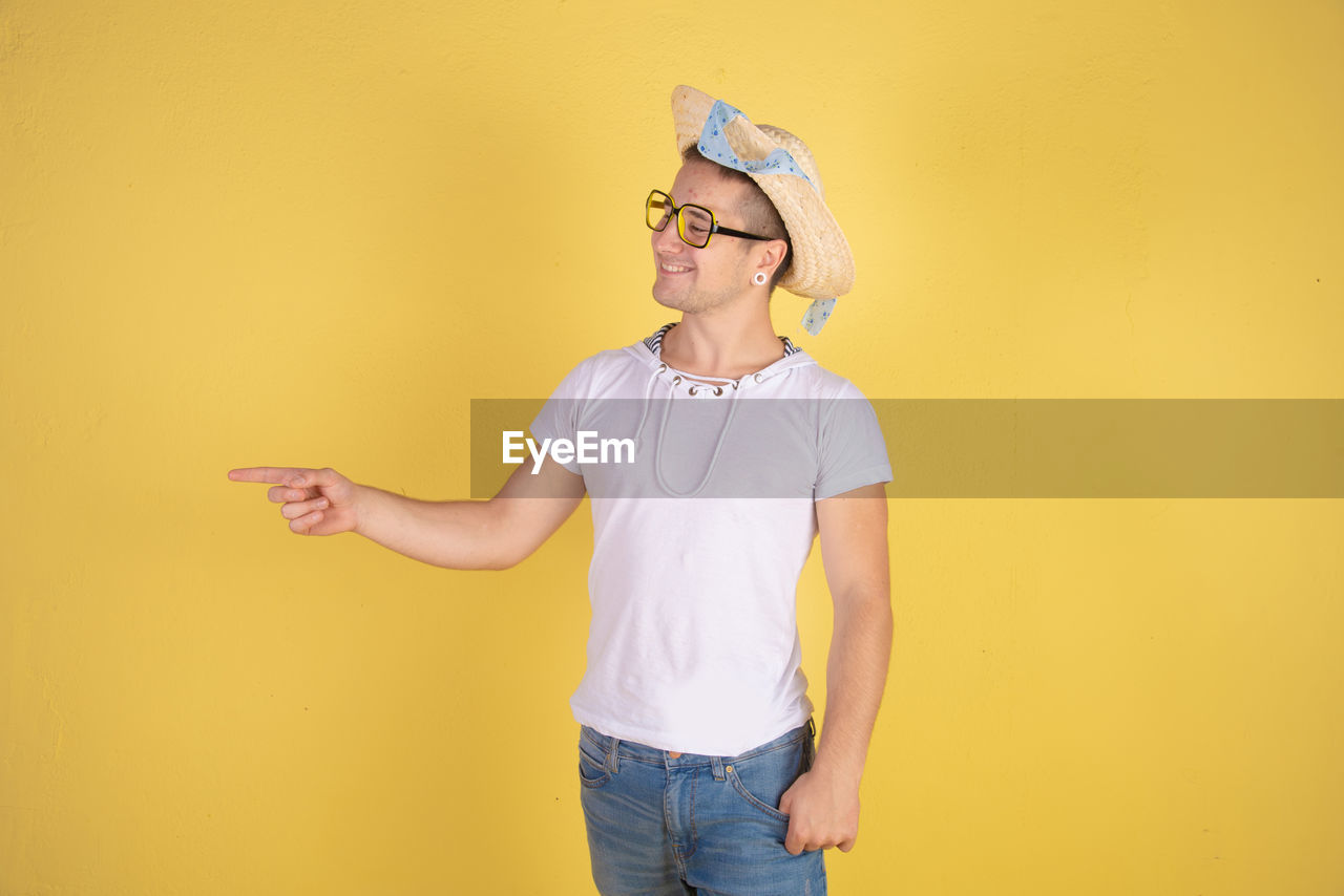 Smiling young man wearing hat standing against yellow background