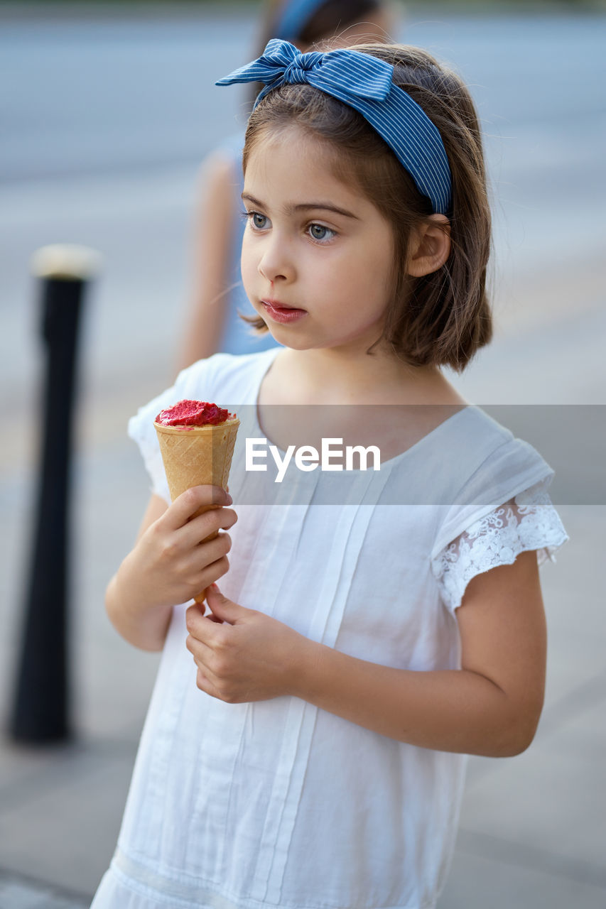 Cute girl holding ice cream cone while standing outdoors