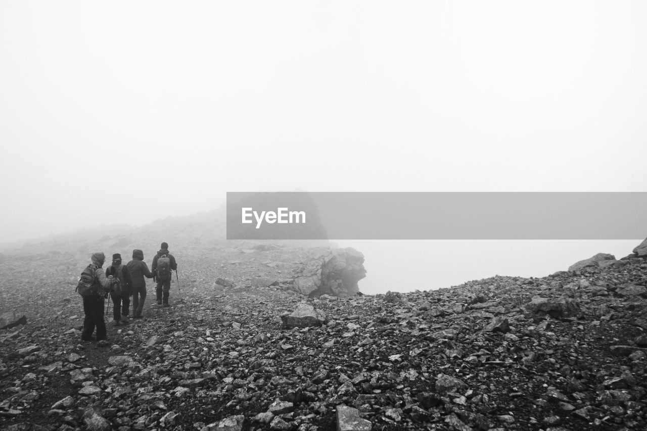 People walking on landscape against sky during foggy weather