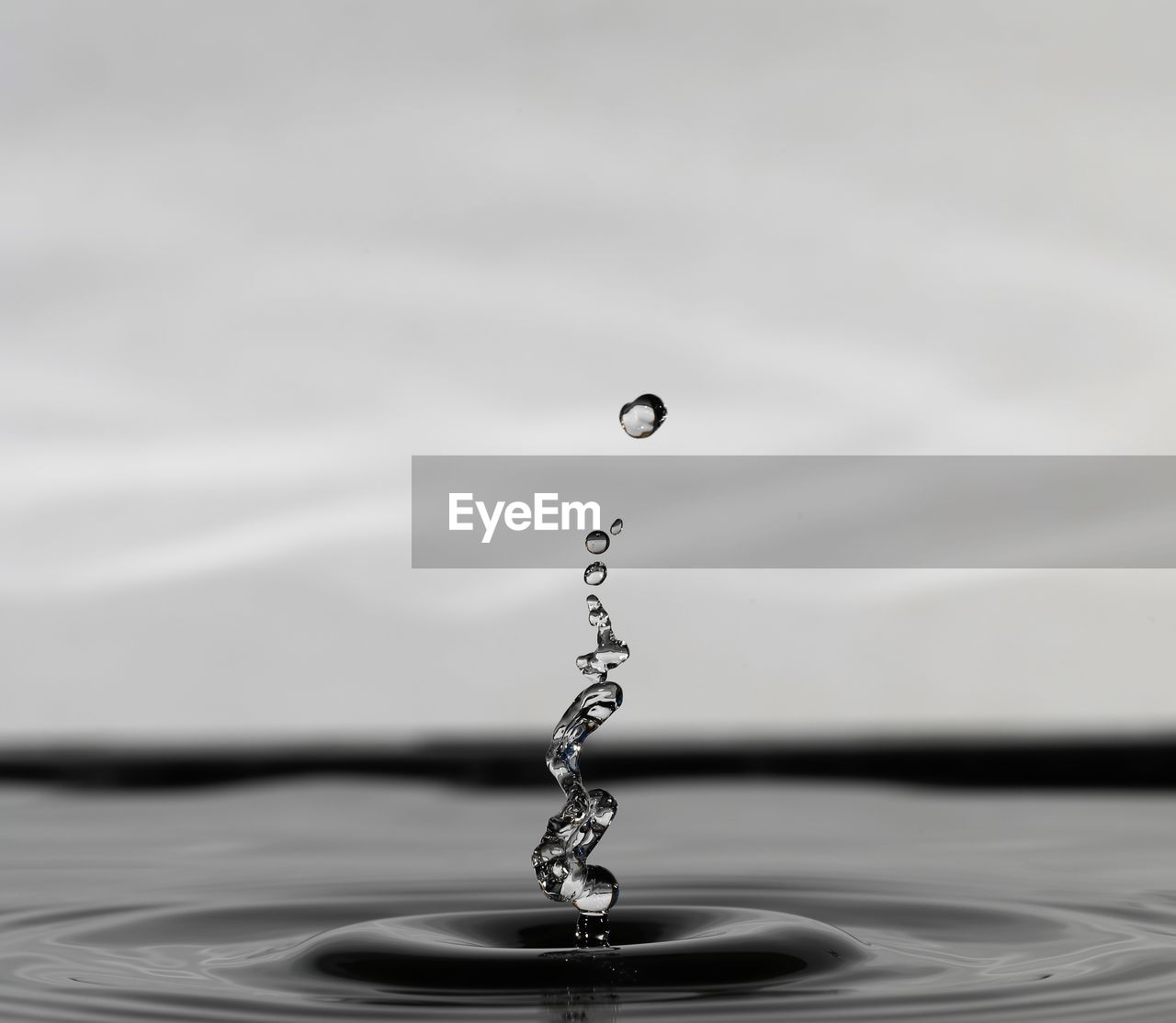 CLOSE-UP OF DROP FALLING ON WATER AGAINST BLURRED BACKGROUND
