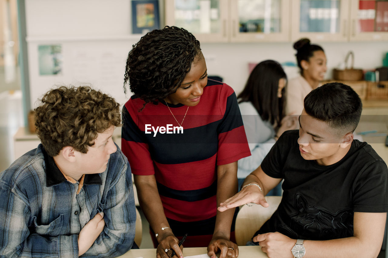 Male student gesturing while discussing with female teacher in classroom