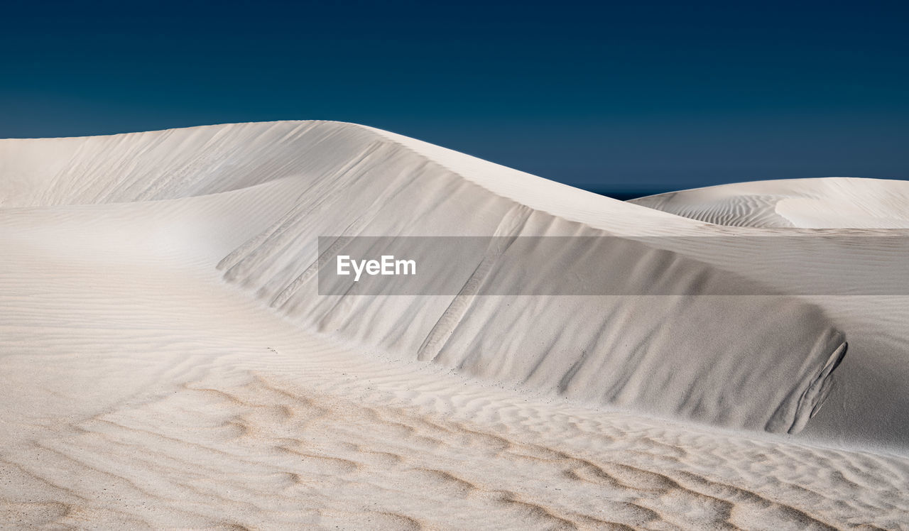 Low angle view of sand dunes against clear blue sky