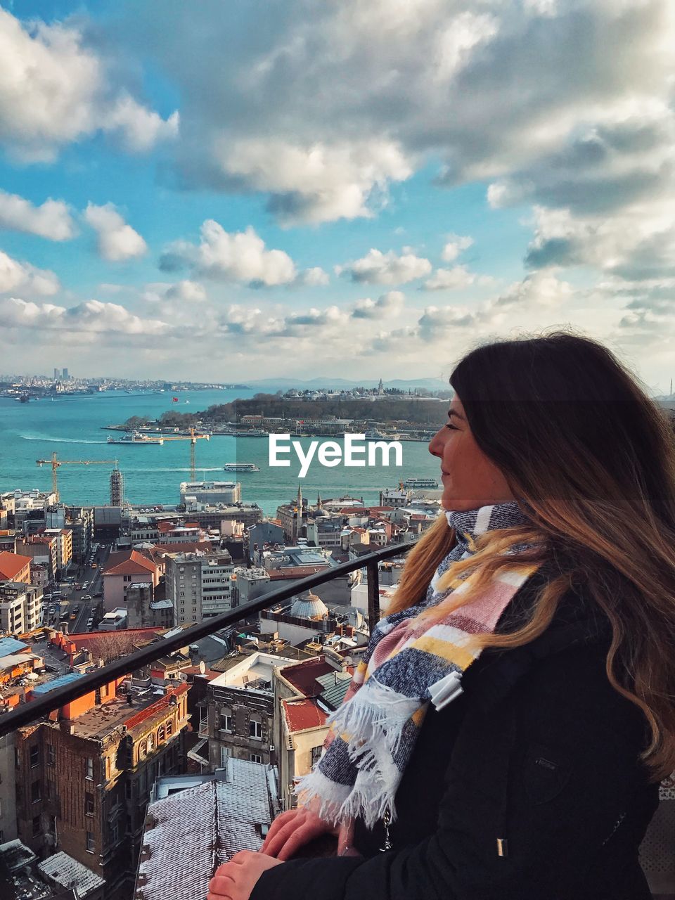 WOMAN LOOKING AT SEA AGAINST CITYSCAPE