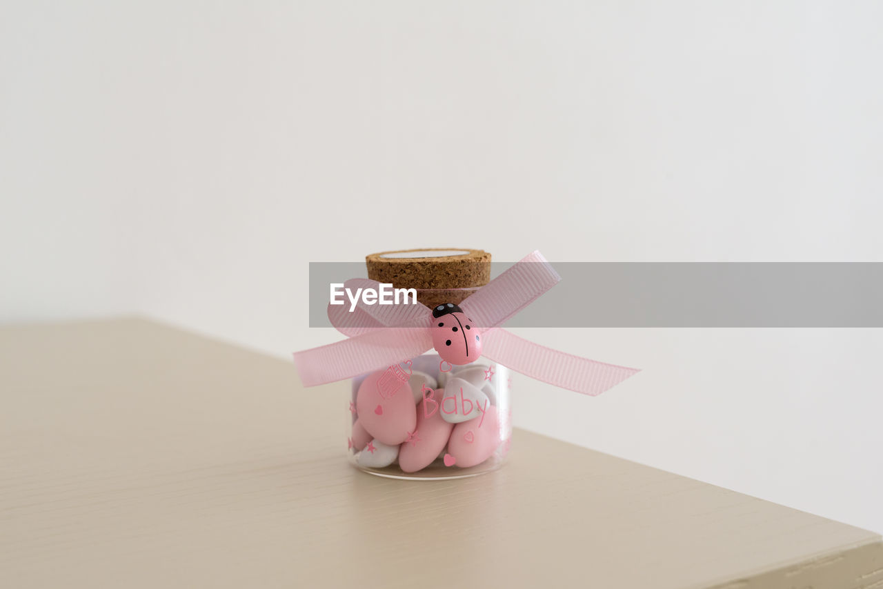Close-up of pebbles in glass bottle tied with ribbon on table against white background