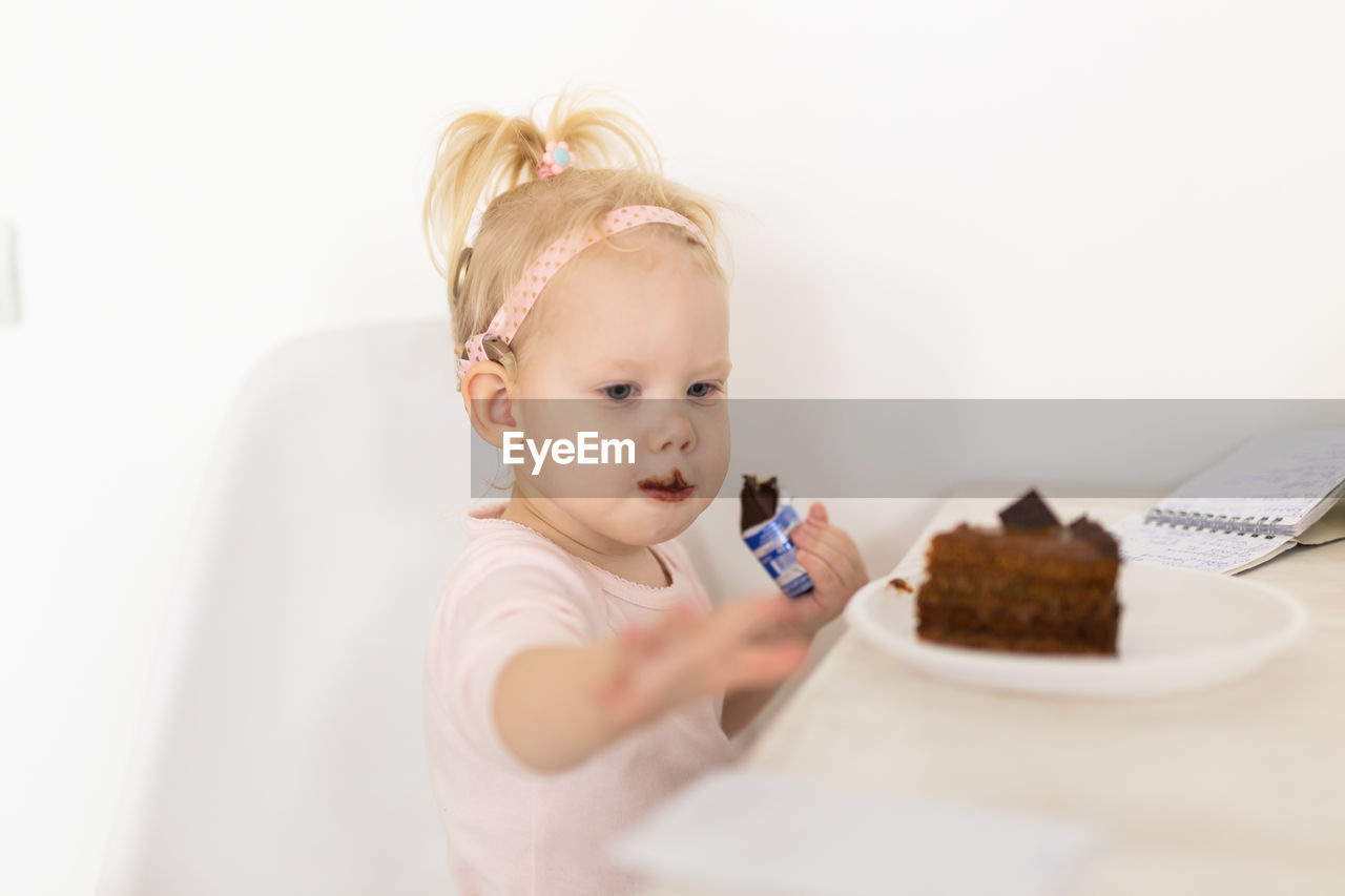 high angle view of cute girl eating food on table against white background