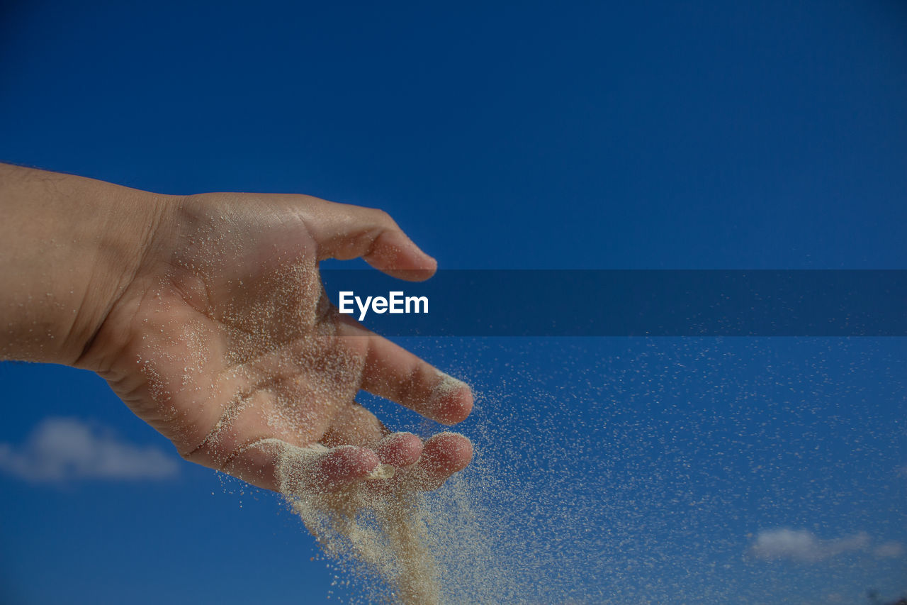 Cropped hand throwing sand against blue sky