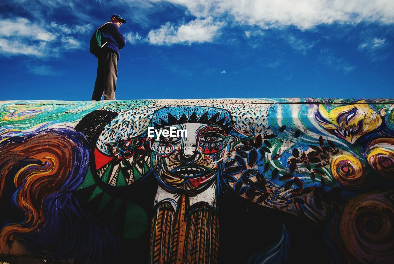 Low angle view of man standing on graffiti wall against sky