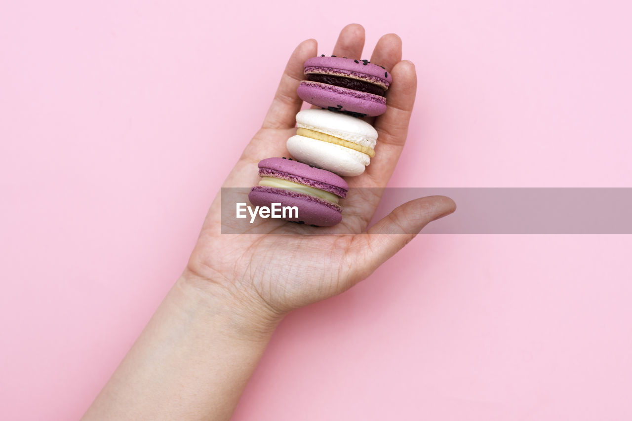 Cropped hand of woman holding macaroons over pink background