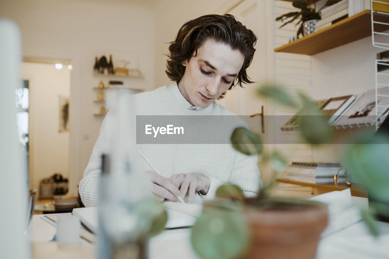 Male entrepreneur writing while sitting at desk in home office