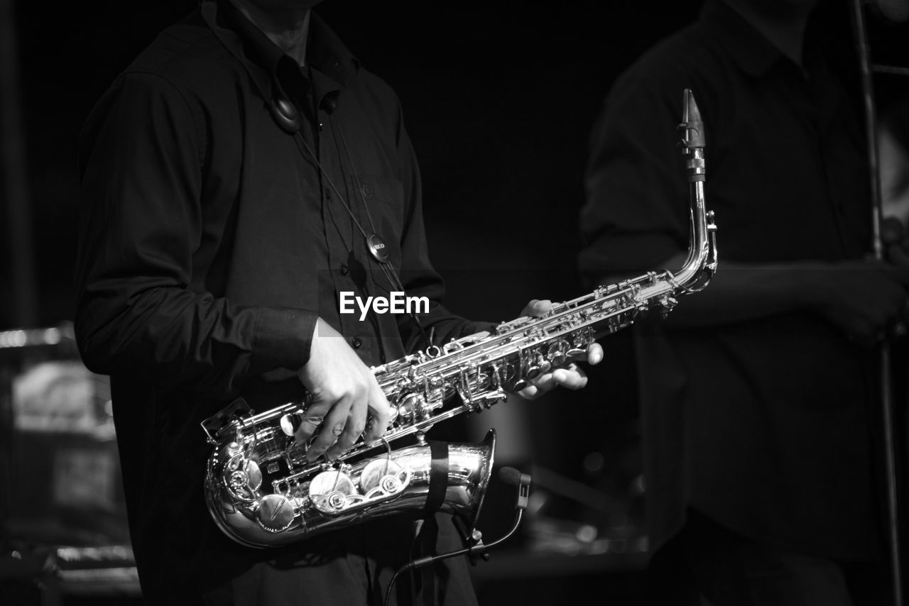 Midsection of man playing saxophone in darkroom