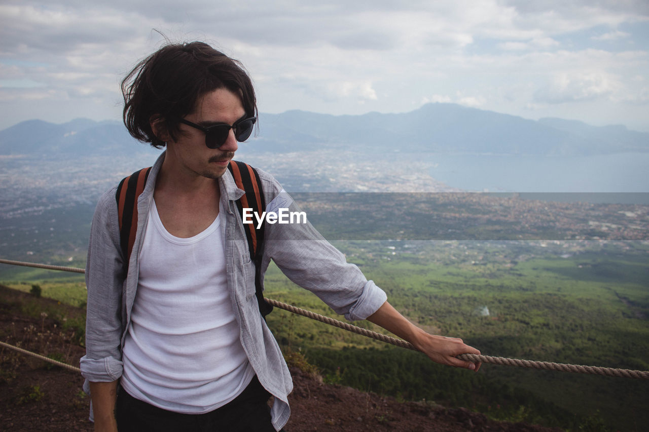 Mid adult man wearing sunglasses standing on mountain against cloudy sky