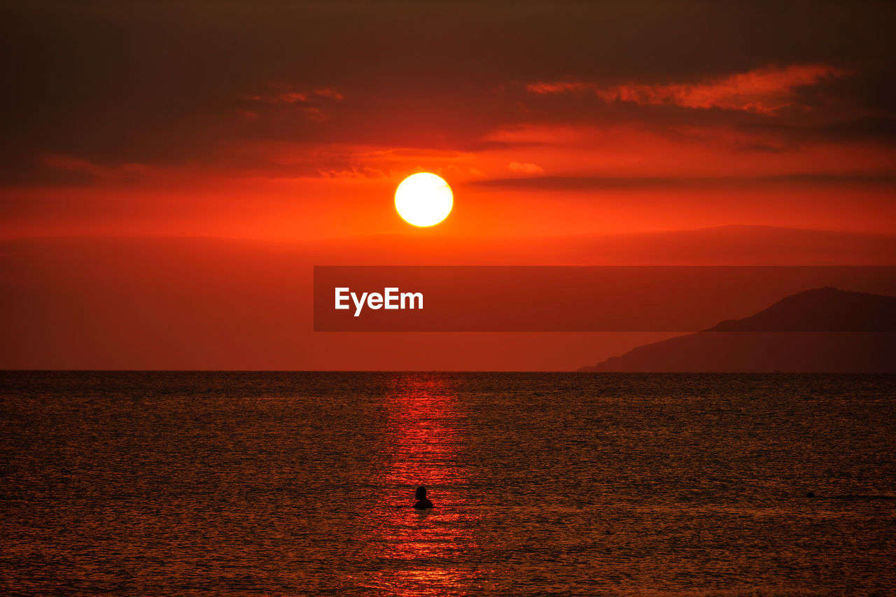Scenic view of sea against orange sky and silhouette of island