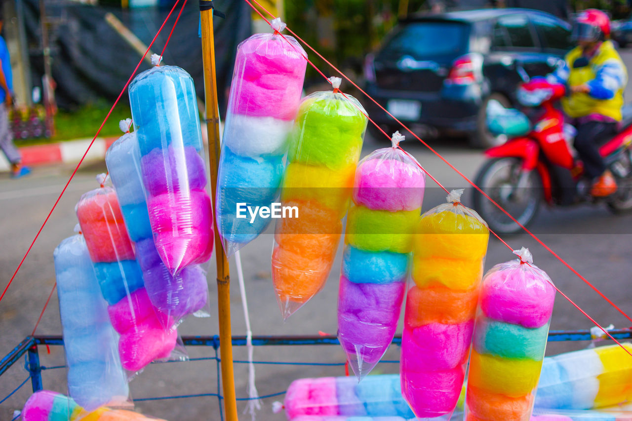 Close-up of colorful cotton candies in plastic hanging from string at street market stall
