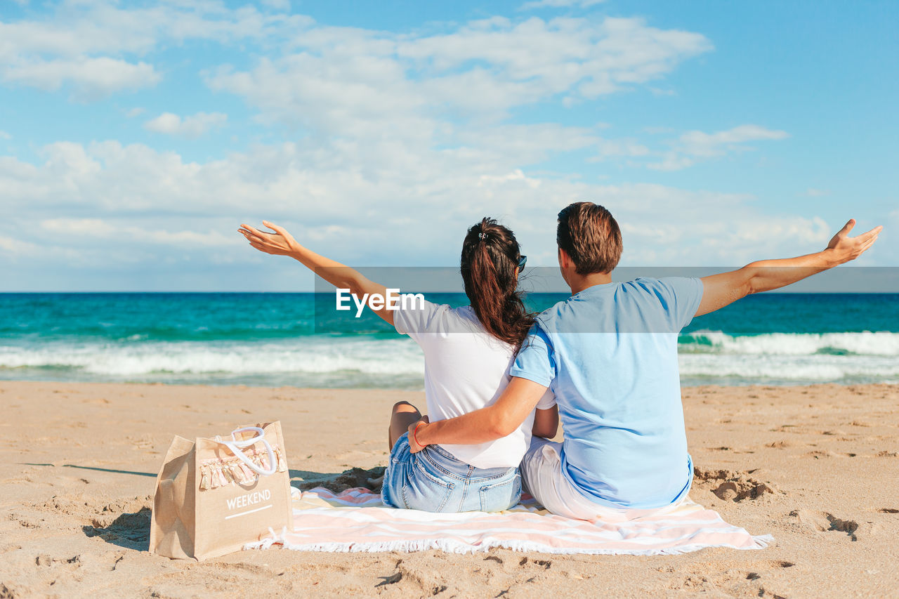 side view of woman sitting on beach against sky