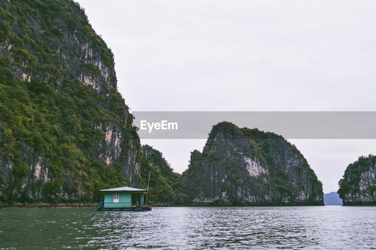 Houseboat by mountain in halong bay against clear sky
