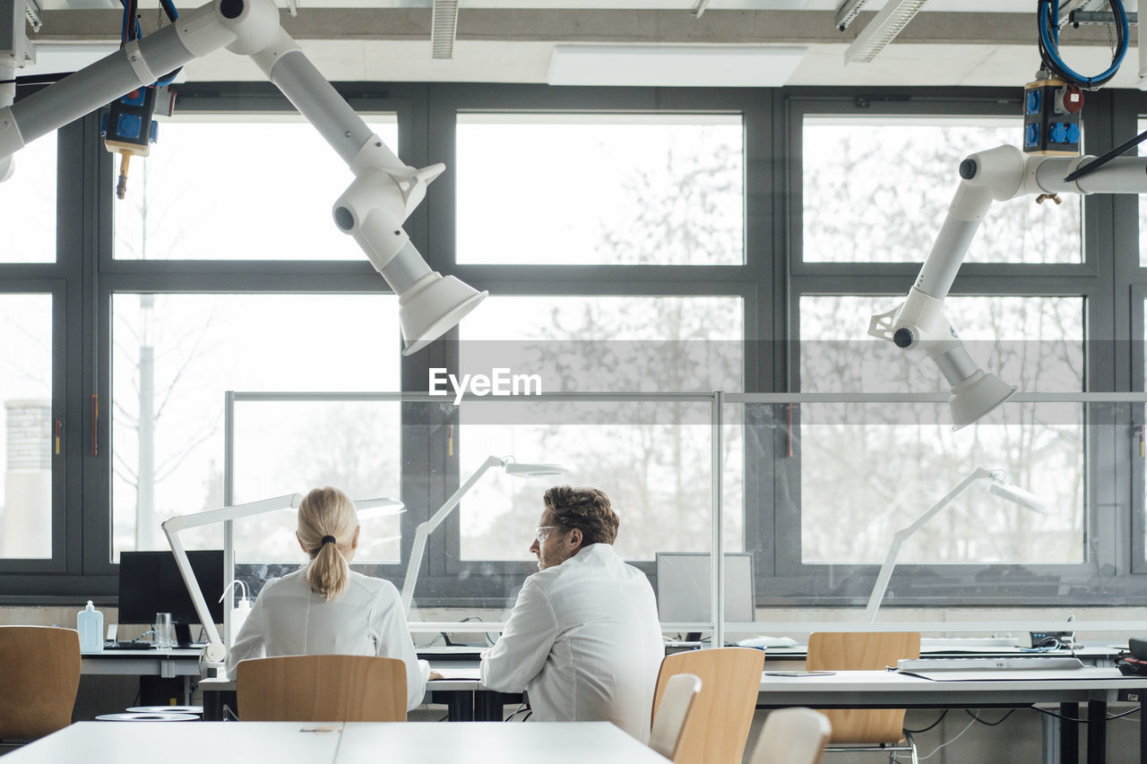 Scientist with colleague sitting at desk in laboratory