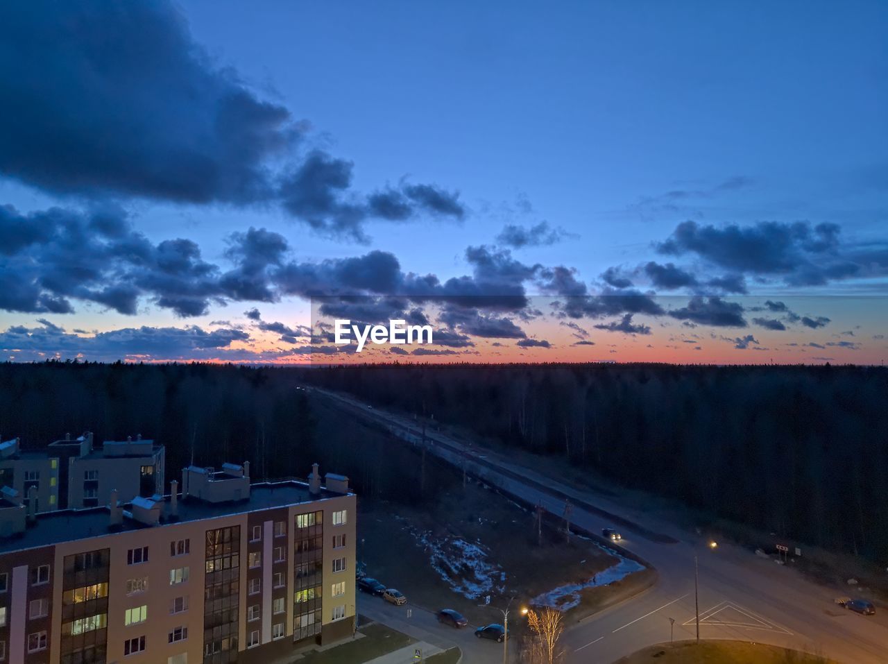 Road by illuminated buildings against sky during sunset