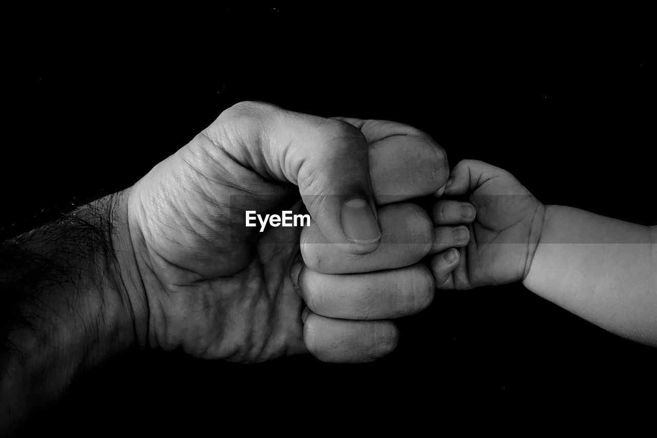 Cropped image of father and child bumping fist against black background
