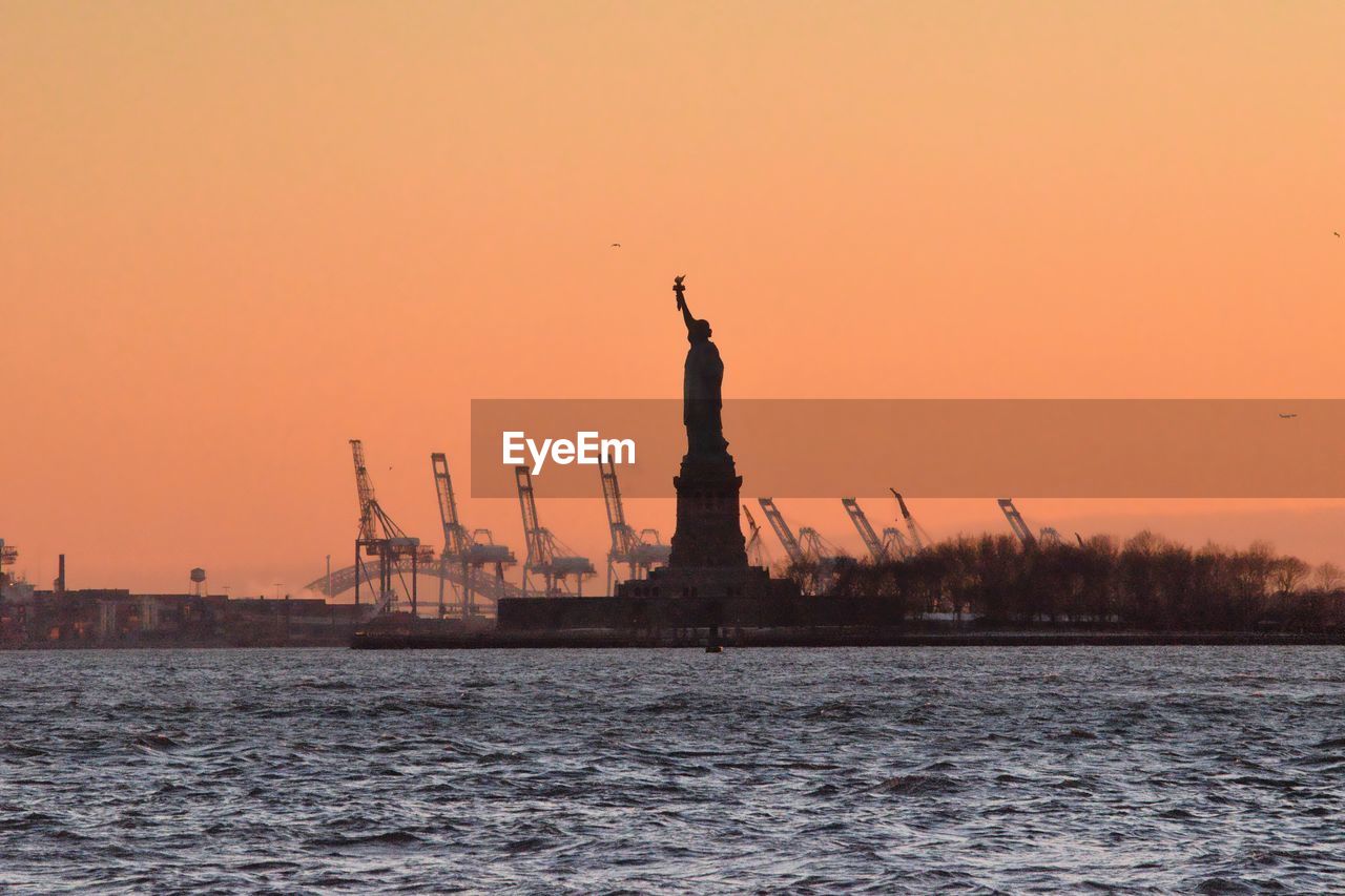 Statue of liberty and sea against orange sky during sunset