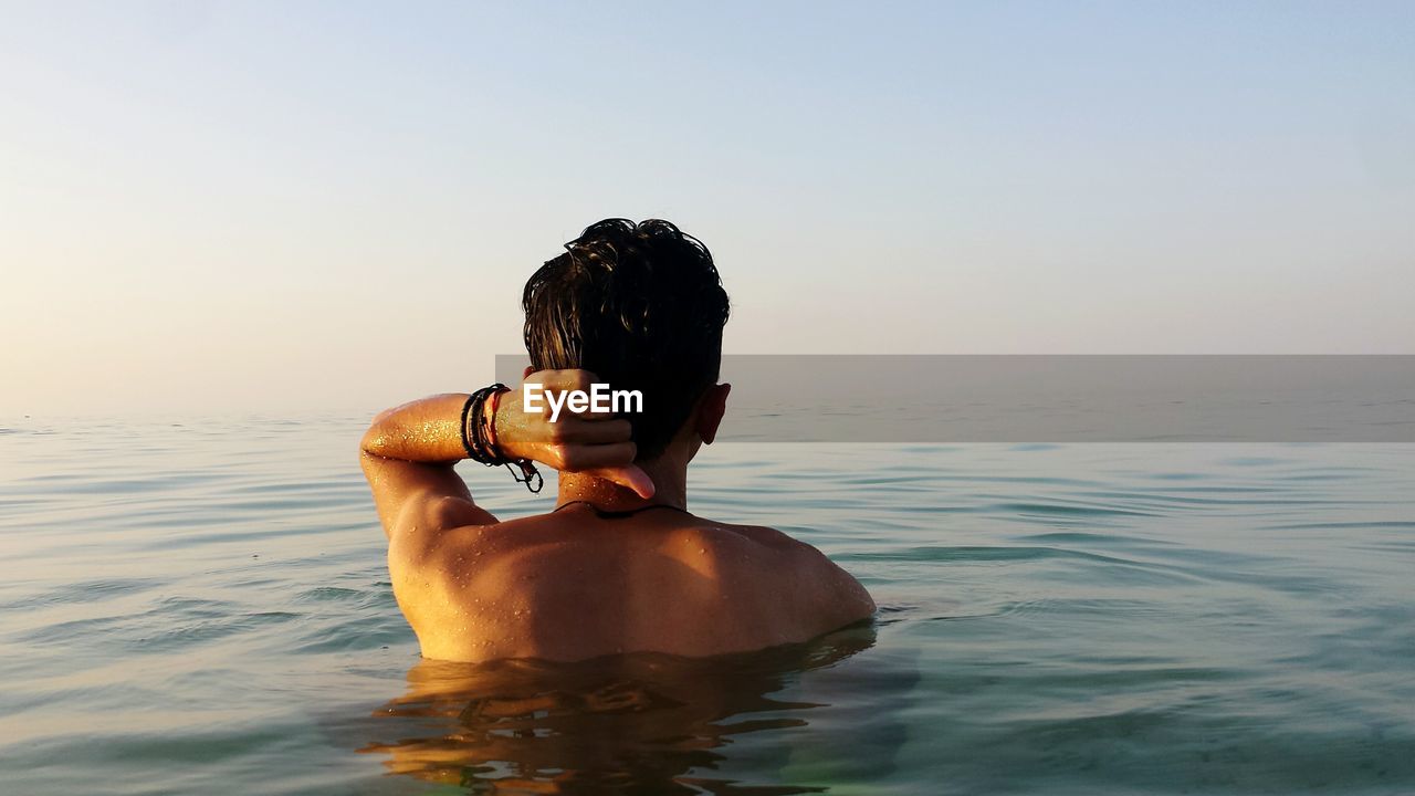 REAR VIEW OF SHIRTLESS WOMAN STANDING IN SEA