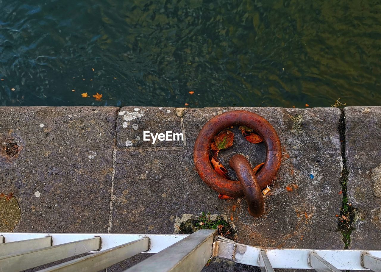 HIGH ANGLE VIEW OF RUSTY CHAIN BY LAKE