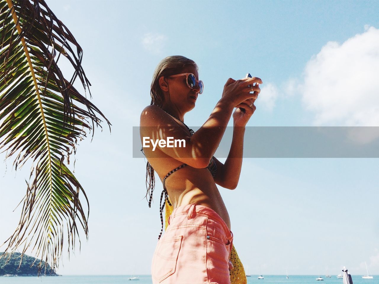 Low angle view of woman using phone at beach against sky