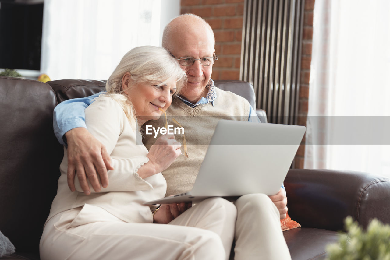 Senior man and woman looking at laptop while sitting at home