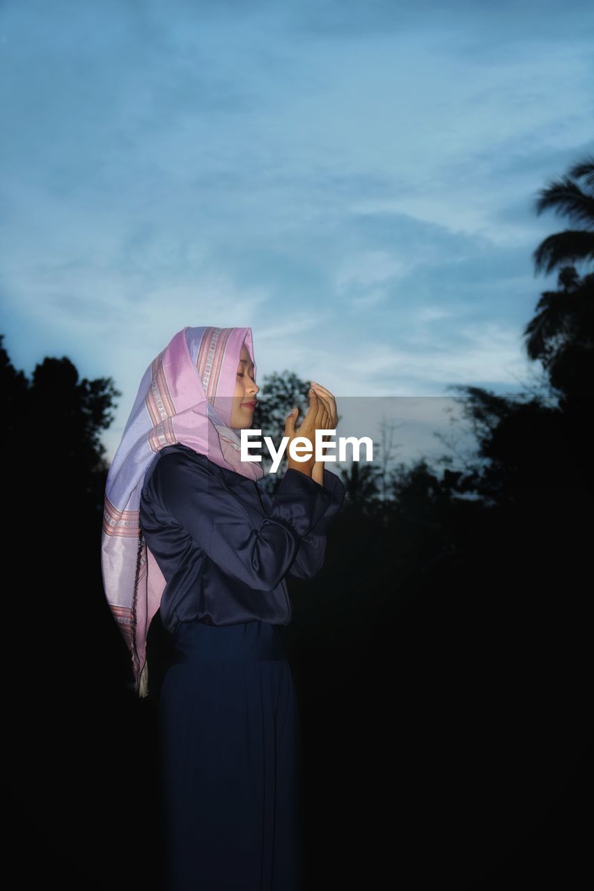 Woman praying on field against sky