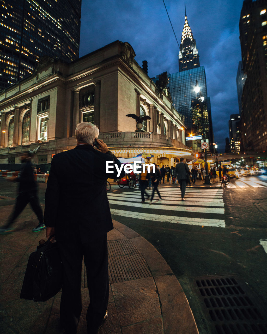 People walking at city street against illuminated buildings during dusk