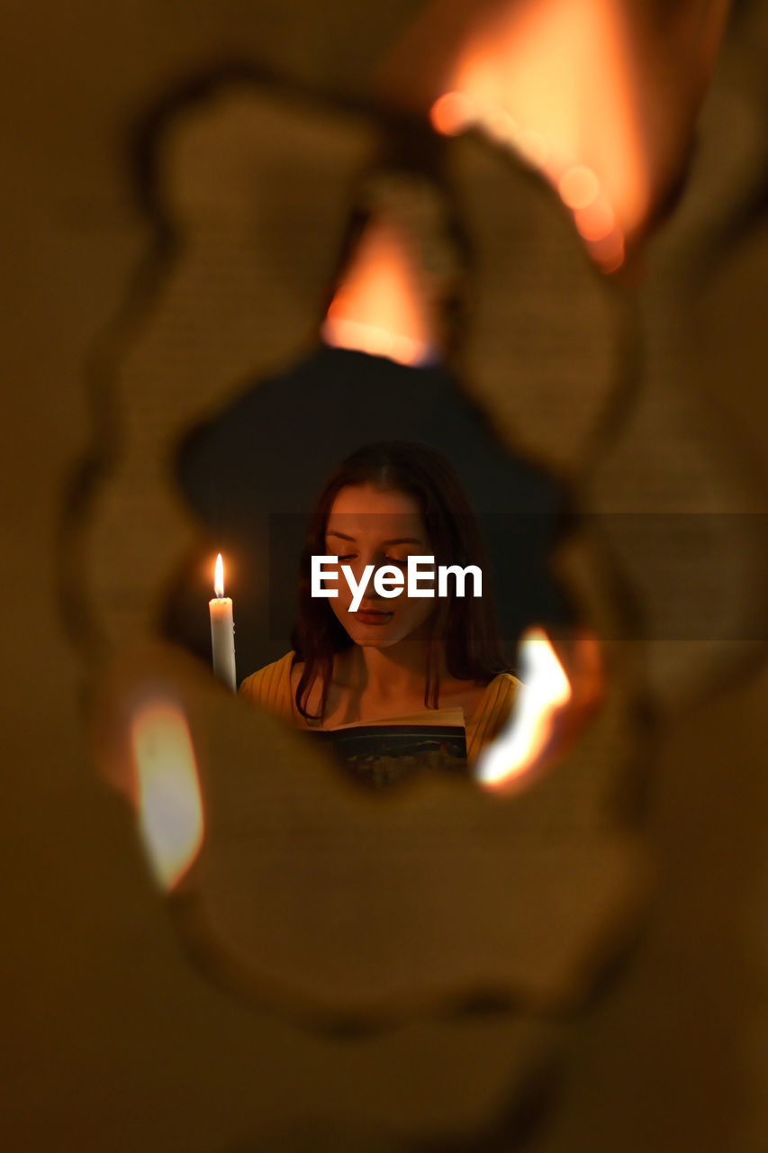 Girl reading book in candle light through flames in dark room