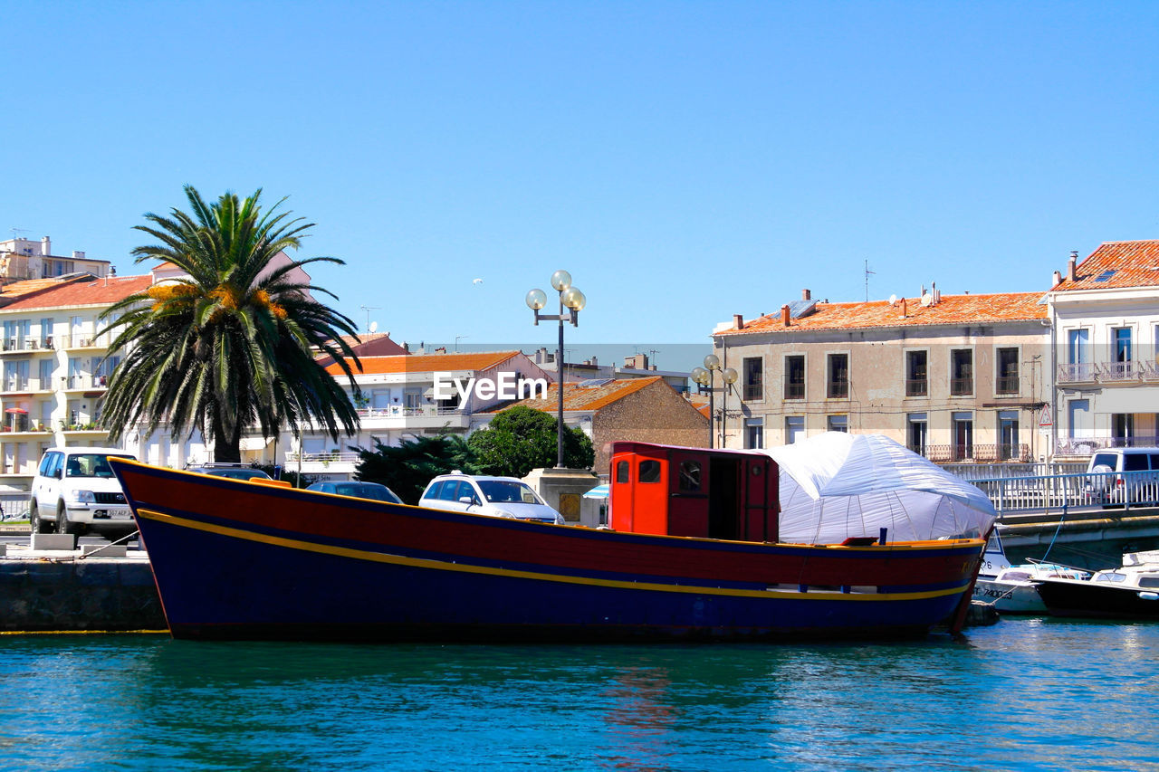 BOATS IN RIVER WITH BUILDINGS IN BACKGROUND