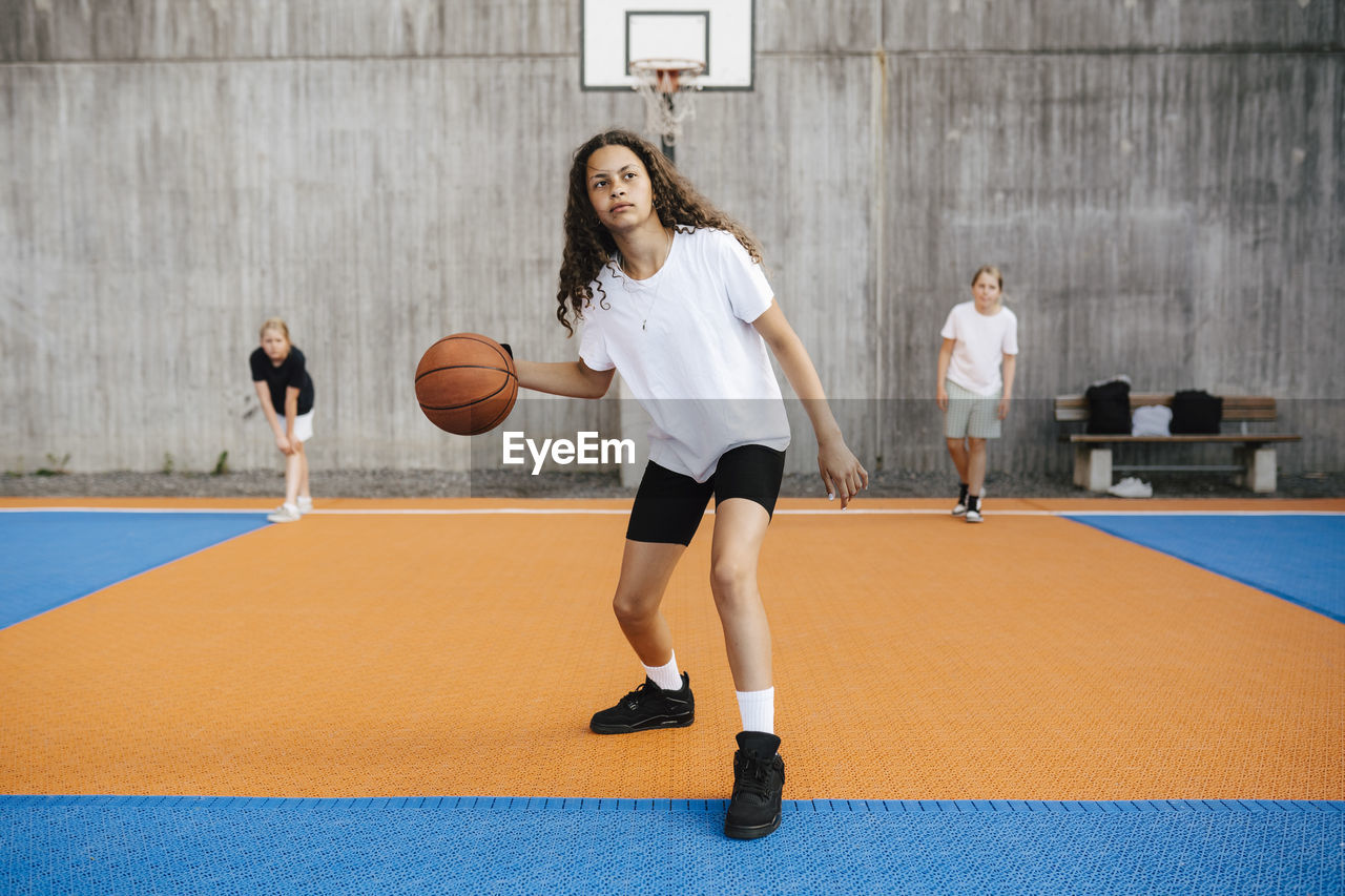 Pre-adolescent girl looking away while practicing basketball in court