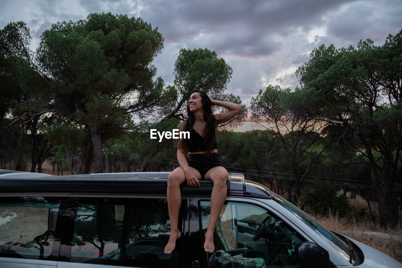 Woman sitting on car against trees