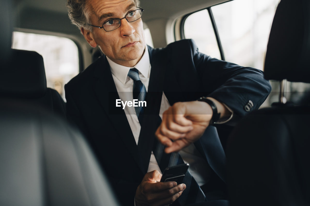 Businessman wearing wristwatch during business trip while sitting in taxi
