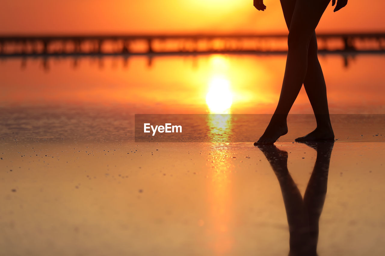 low section of silhouette woman walking on beach during sunset