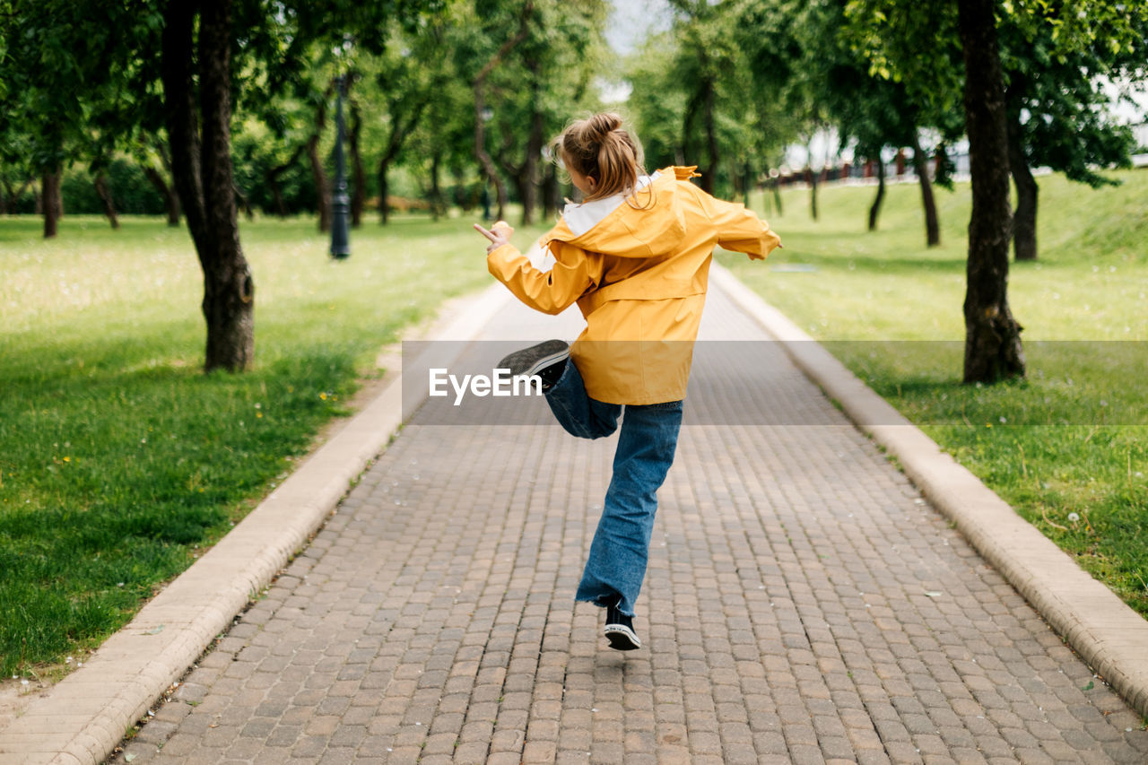 A teenage girl walking in the park jumping with ice cream in her hands. view from the back.