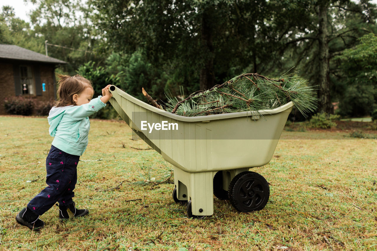 Side view of girl holding wheelbarrow on field