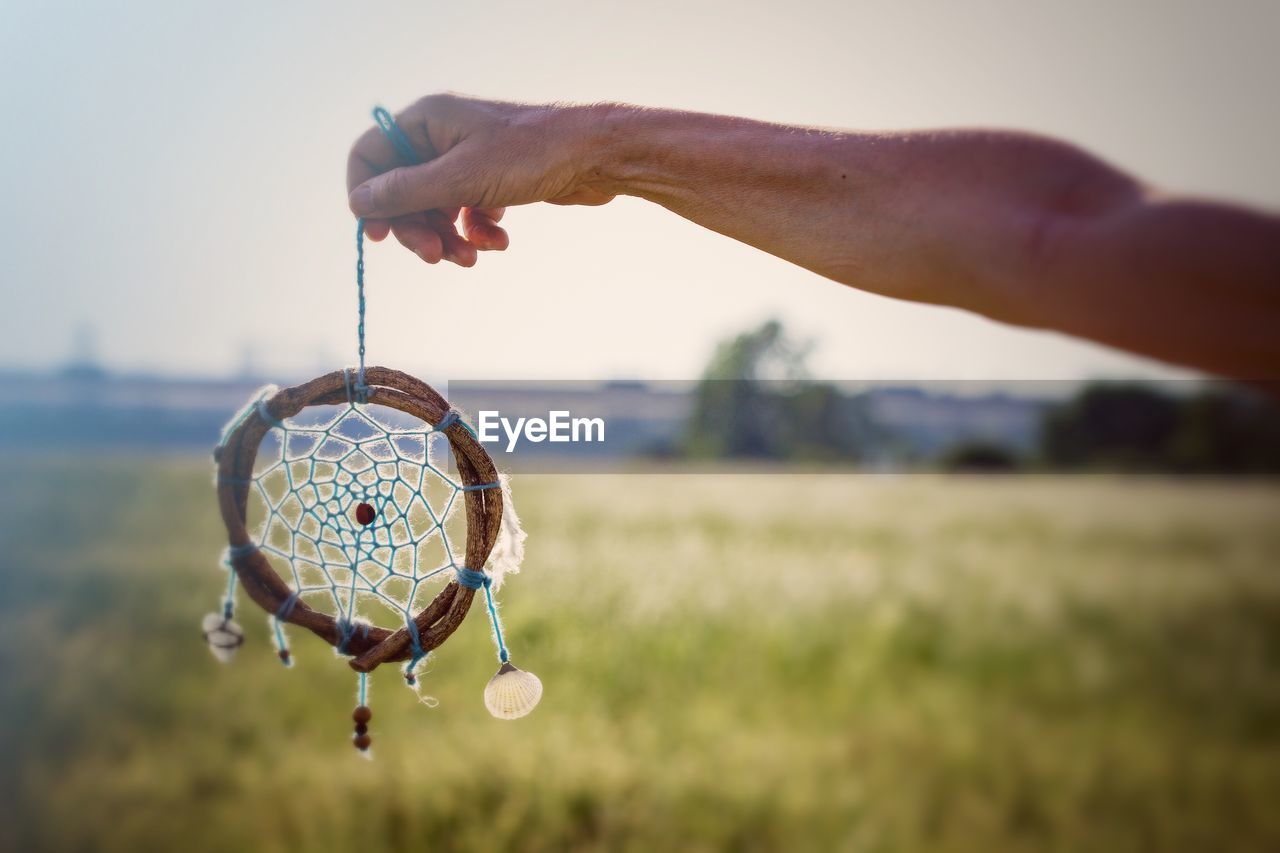 Cropped hand holding dreamcatcher on field