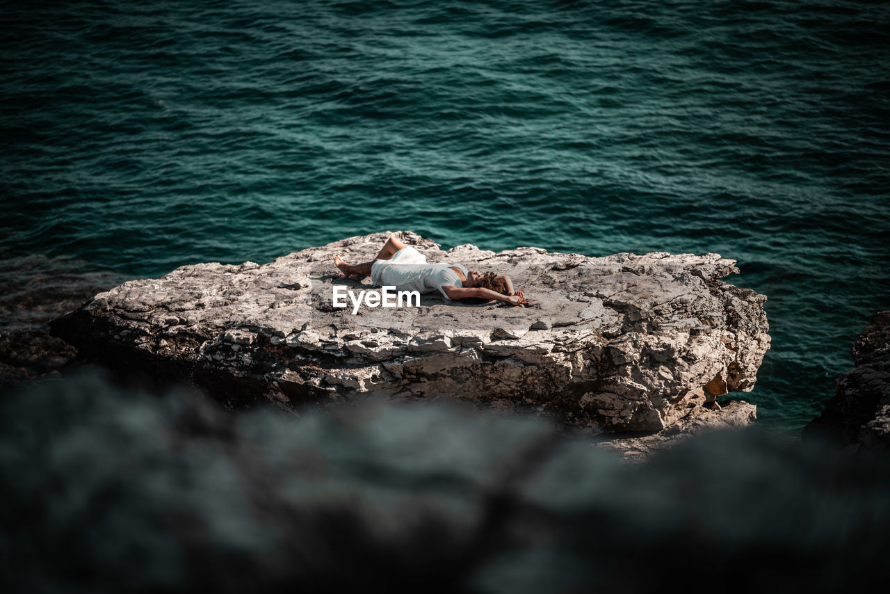 High angle view of woman lying cliff against sea