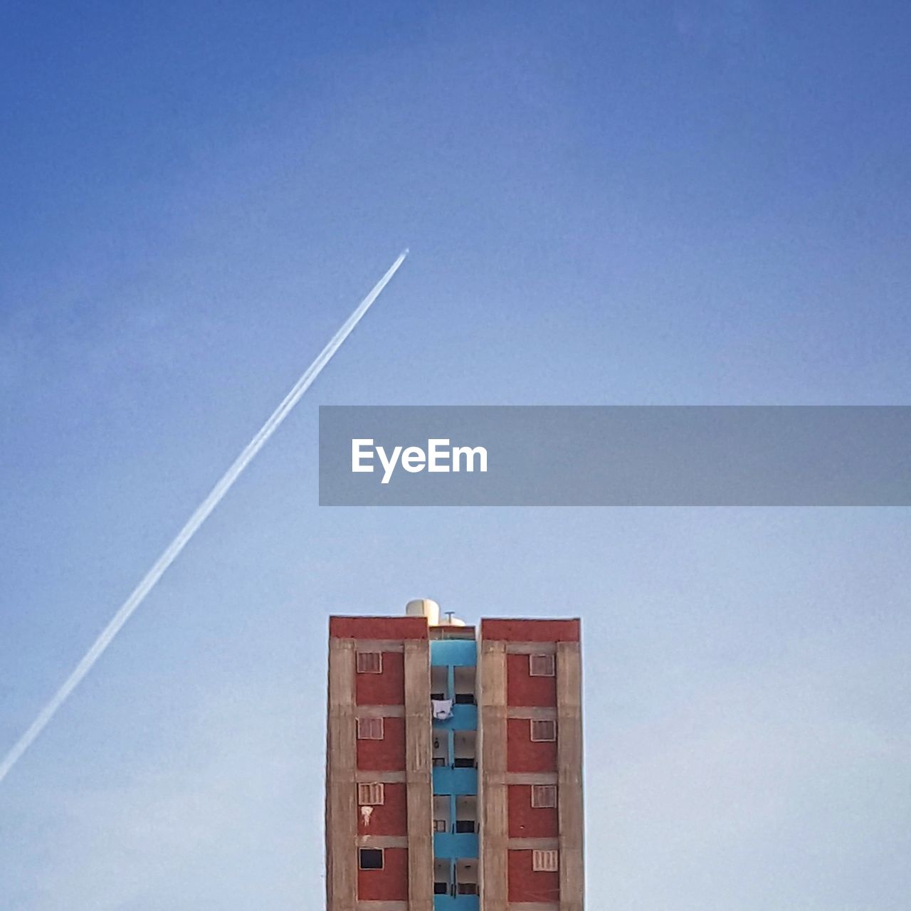 Low angle view of vapor trail and residential building against clear blue sky
