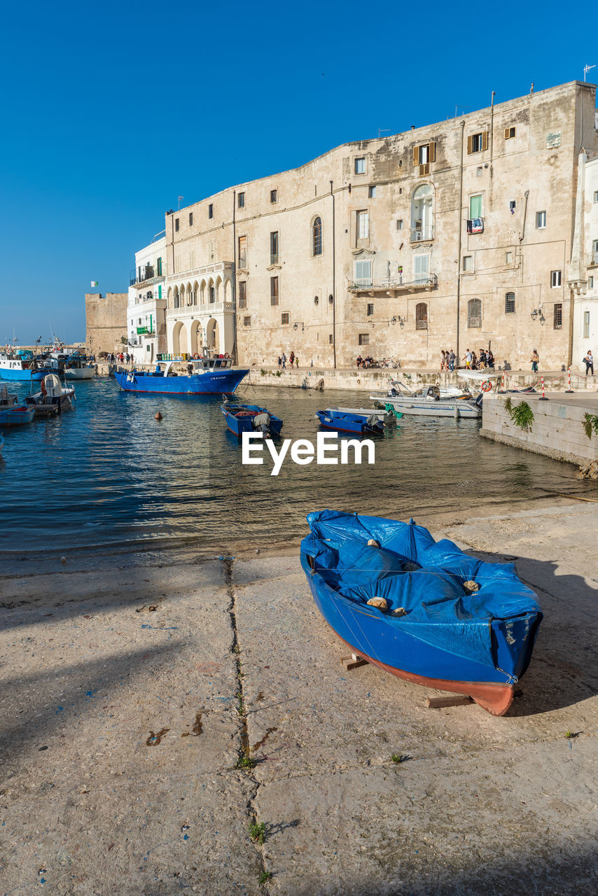 BOATS MOORED IN CANAL BY CITY BUILDINGS AGAINST CLEAR BLUE SKY