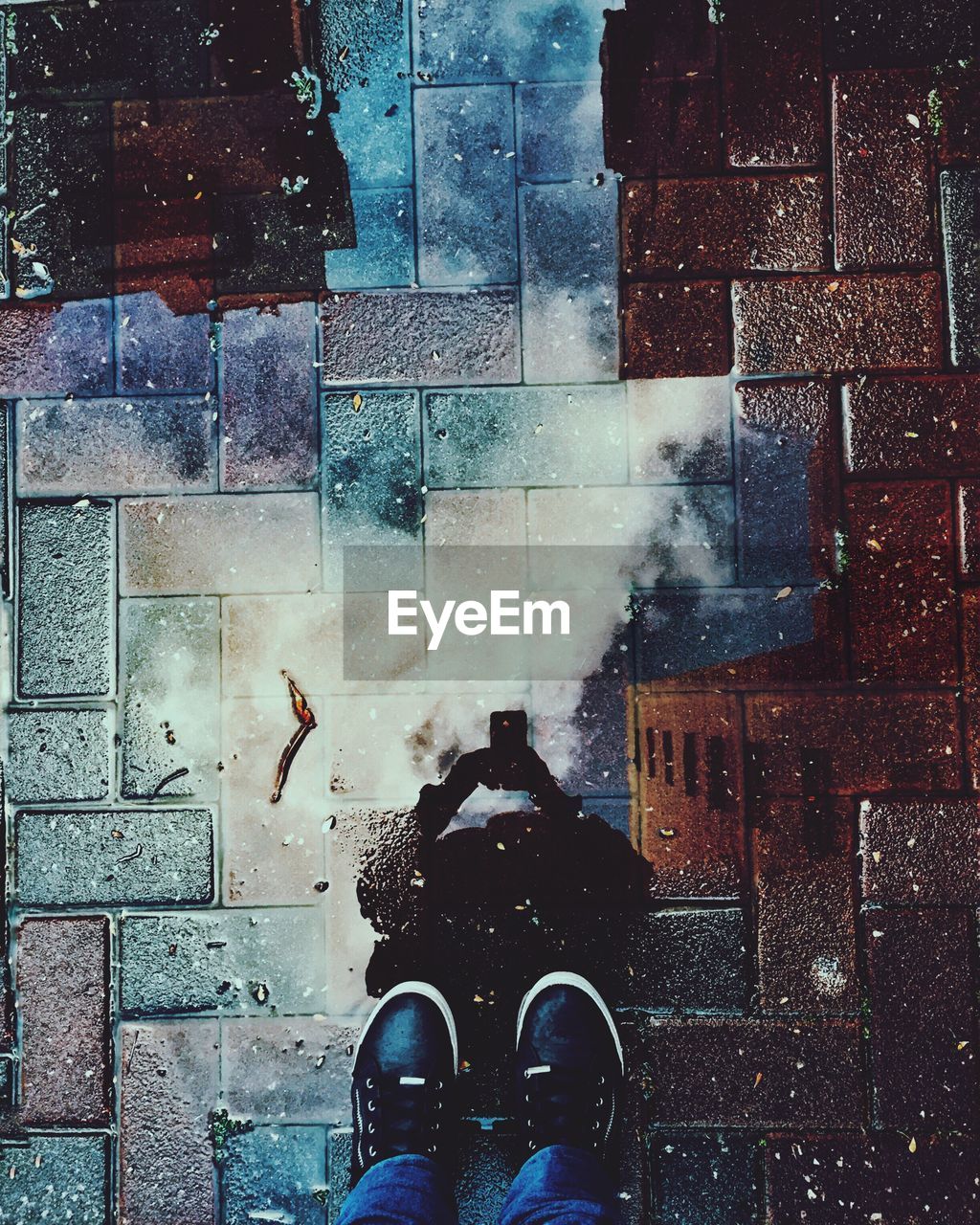 Person reflecting in puddle while standing on wet footpath