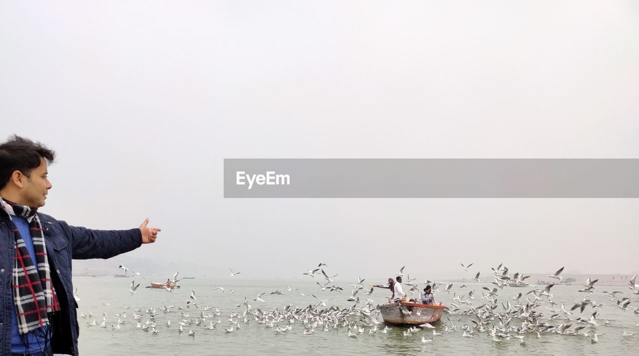 SIDE VIEW OF MAN STANDING IN SEA AGAINST SKY