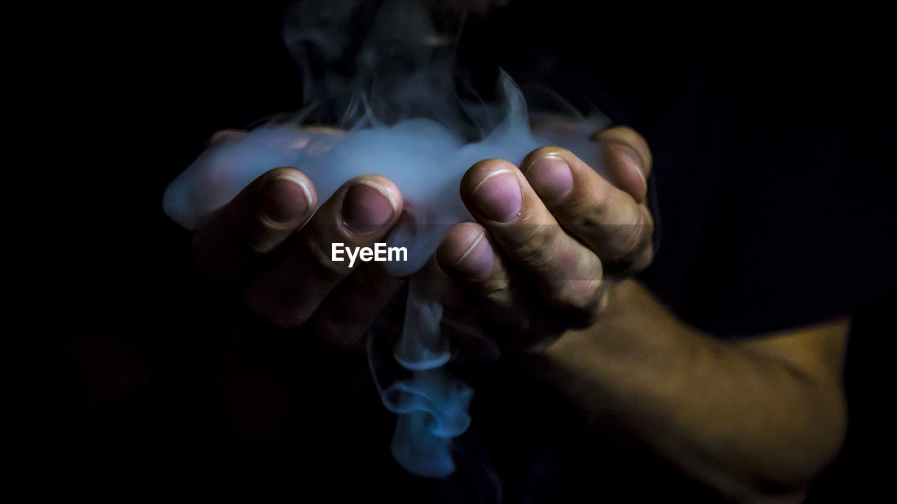 Cropped hands with smoke against black background
