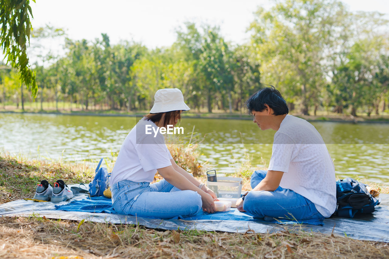 Asian couple picnic with happiness feeling in park with lake in springtime